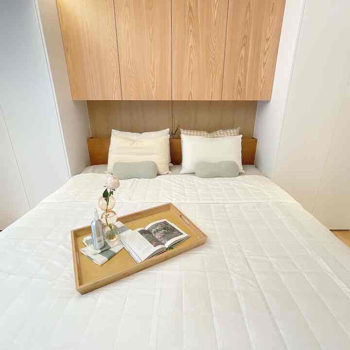 Bright bedroom for two with white and natural wood tones, featuring a bed with a wooden tray centered, conveying a fresh summer bedding atmosphere
