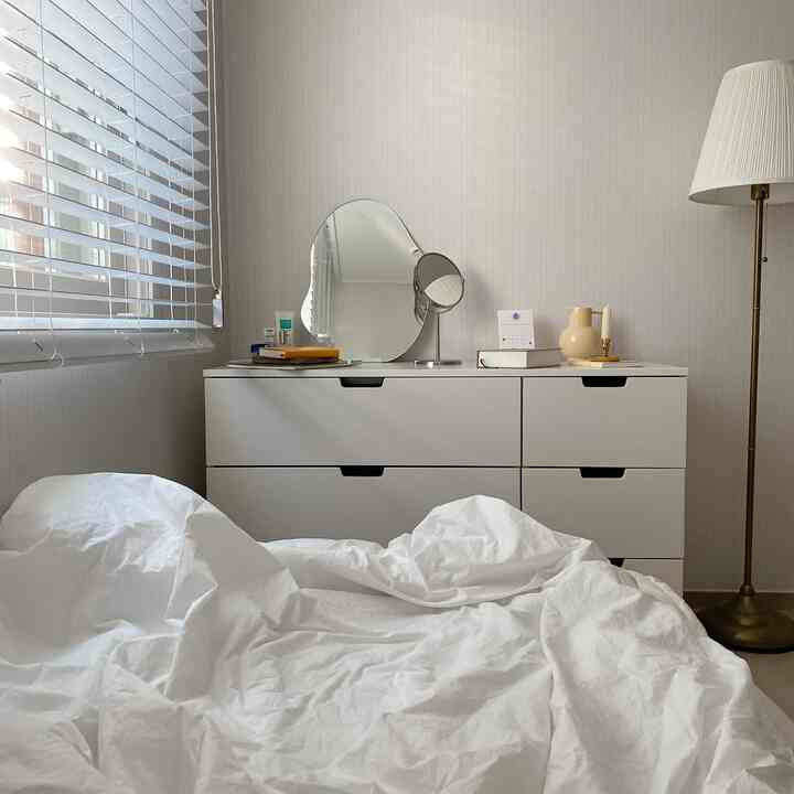 明るいホワイトトーンの寝室、ドレッサーを化粧台として活用し、鏡とフロアランプが配置されたすっきりとしたインテリア