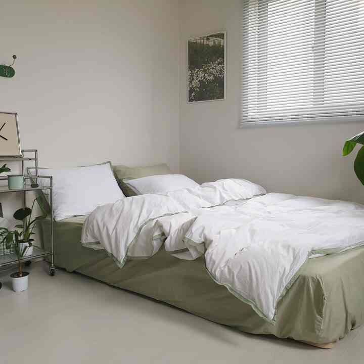 ナチュラルな色調の寝室、白い掛け布団カバーと緑の寝具が配置された落ち着いた空間