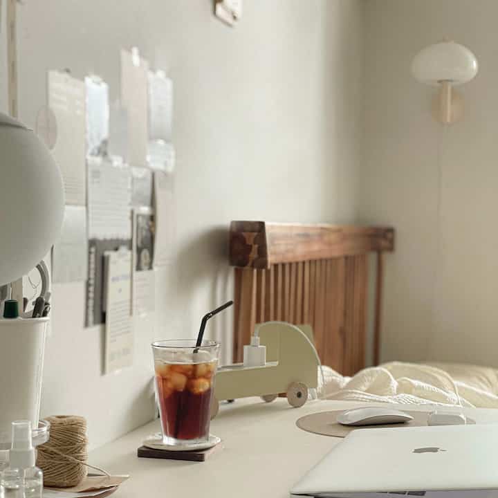 A white and wood tone bedroom featuring a simple desk, bed frame, and cozy home office setup