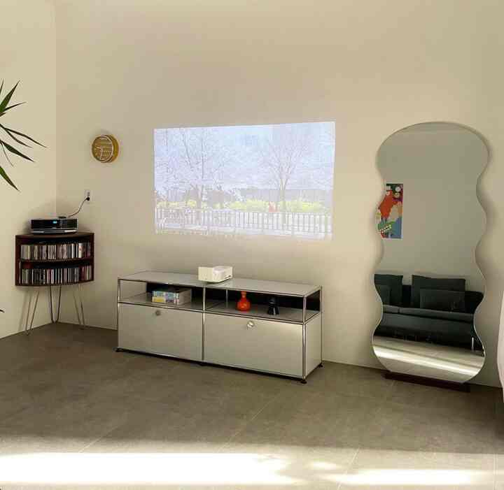 Bright white and natural-toned living room featuring modern cabinet and large full-length mirror, creating a minimal and home cinema atmosphere