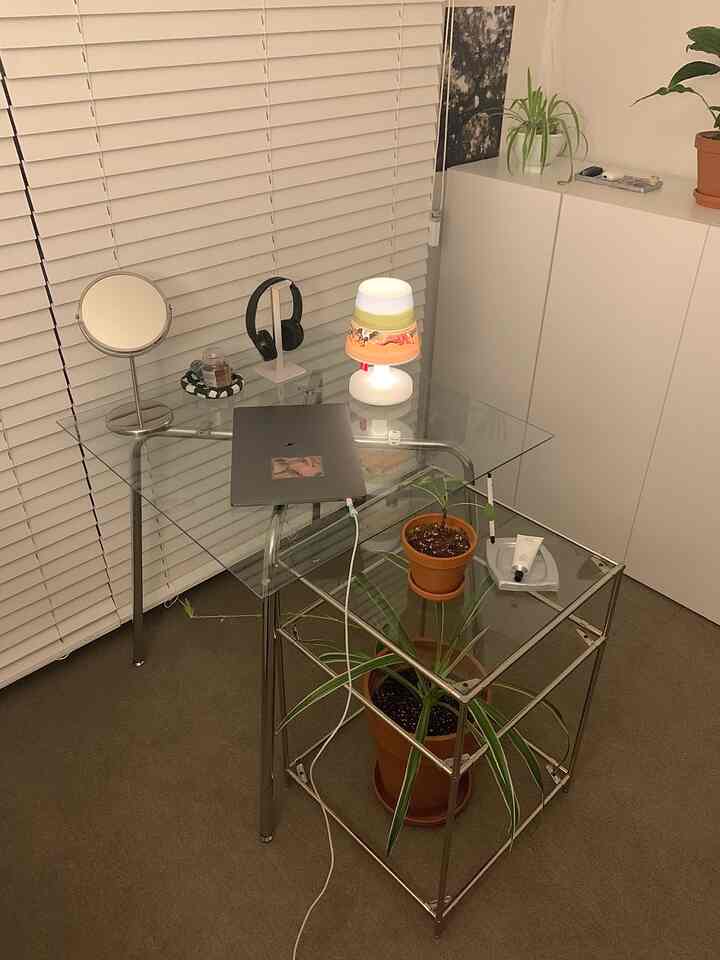 Simple study space featuring white blinds, a transparent table, and plants, creating a clean atmosphere