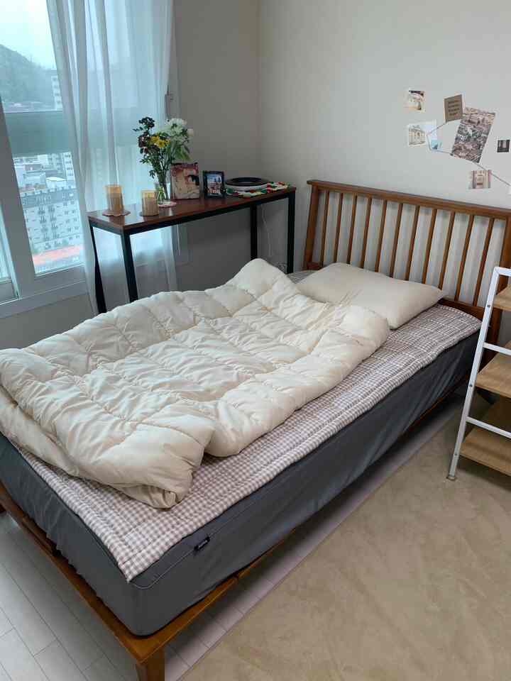 ホワイトのカーテンとブラウンの木製ベッドが置かれたナチュラルな雰囲気のある寝室