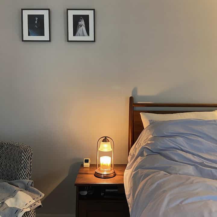 濃いブラウンの木製ベッドとナイトテーブルに温かいキャンドルウォーマーが配されたナチュラルな寝室のインテリア