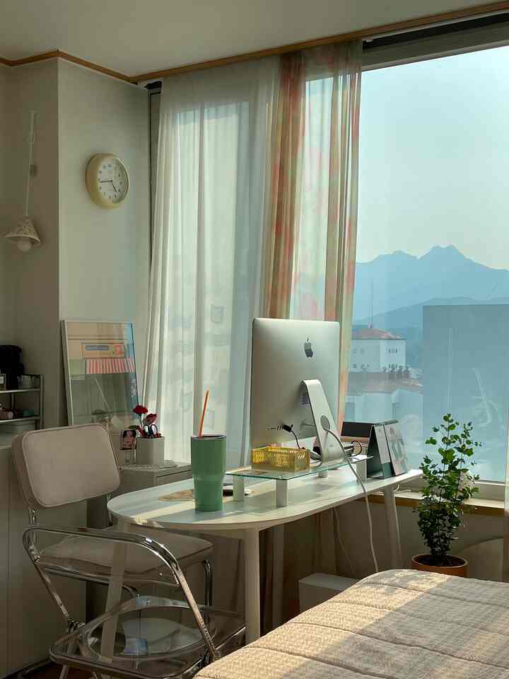 Bright white and transparent-toned studio home office featuring floral curtains on large windows and a computer desk in a cozy setting