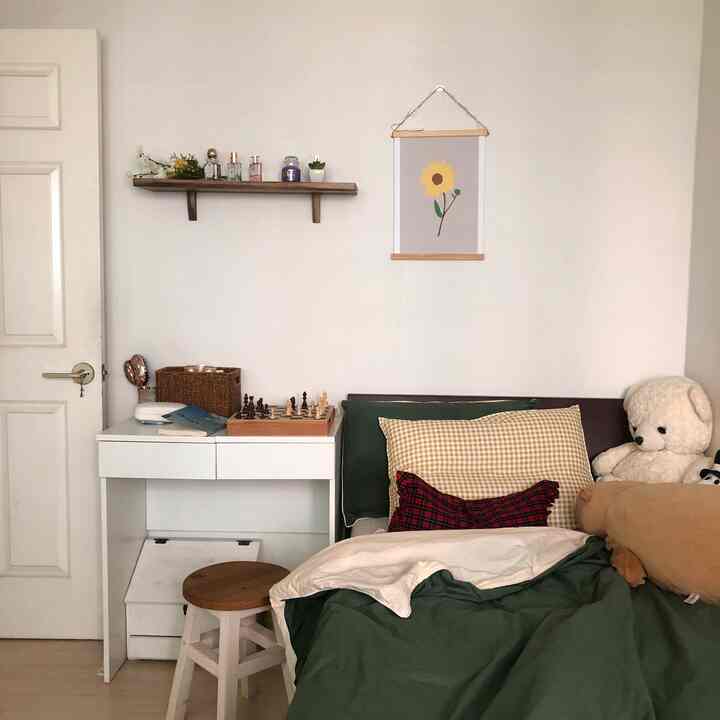 Small bedroom with white walls and furniture, featuring green bedding and simple storage elements conveying a cozy atmosphere