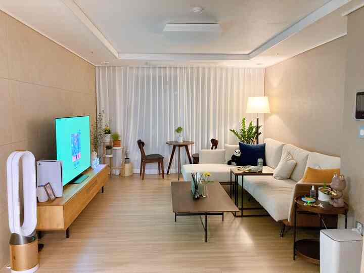 A white and wood tone living room featuring an L-shaped sofa, coffee table, floor lamp, and plants with a natural atmosphere