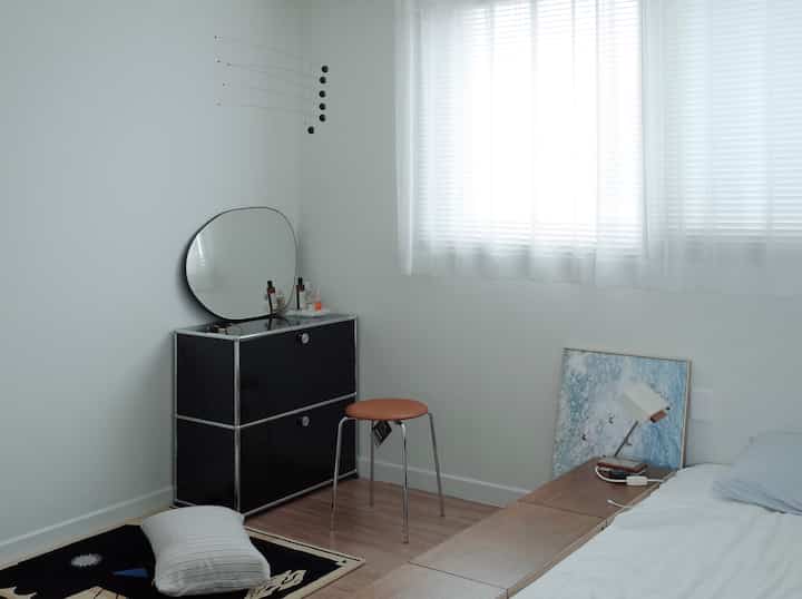 ホワイトとウッドトーンの寝室、ブラックの化粧台とブラウンのスツールが配置された雰囲気のあるナチュラルモダンなインテリア