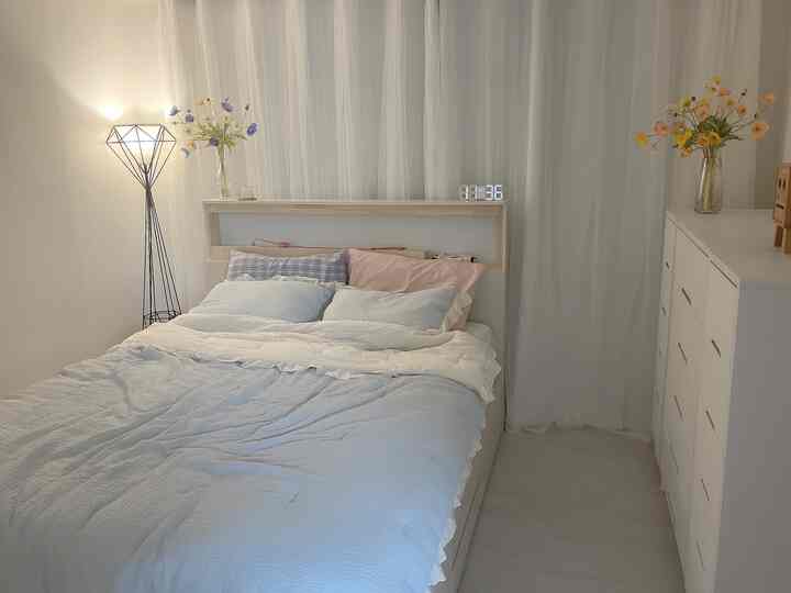 落ち着いた明るいホワイトとナチュラルウッドの寝室、快適なベッドとフロアランプ、造花が配置された居心地の良いインテリア