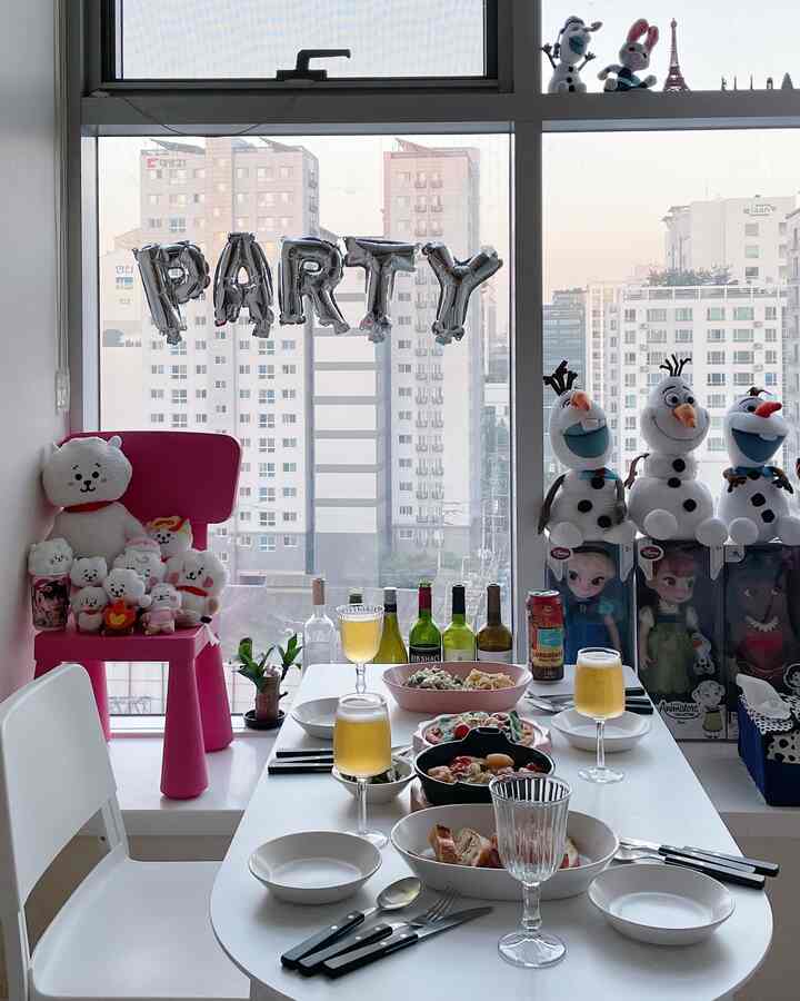 白とピンクの色調のダイニング、窓際のテーブルに食事とワイングラスが配置された雰囲気のあるホームパーティー空間