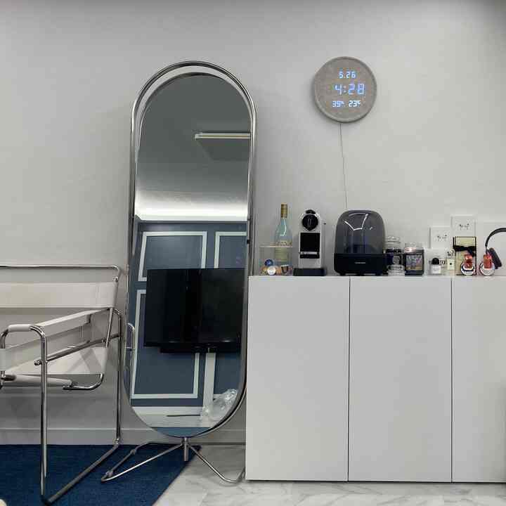 White and blue toned studio apartment featuring a full-length mirror and cabinet topped with coffee machine and Bluetooth speaker, clean modern space