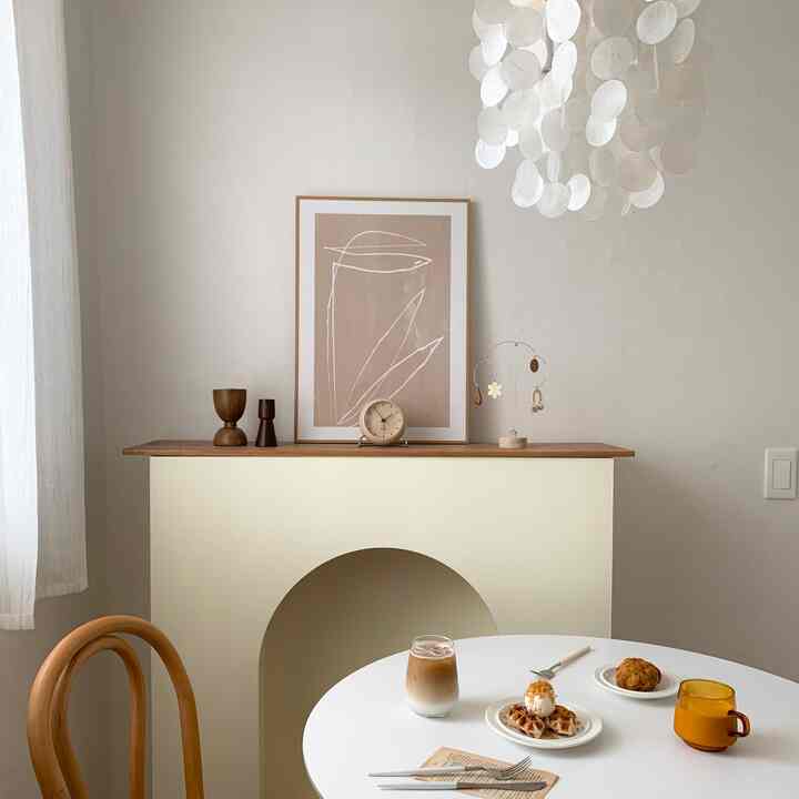 白と茶色のトーンのワークスペース兼ホームカフェ、丸いテーブルとアルネ・ヤコブセンの時計が配置されたシンプルで自然なインテリア