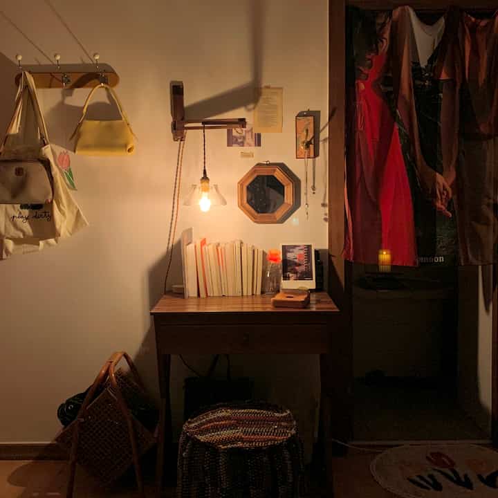 暖かい黄色い照明と木目調のアットホームな小さな部屋、壁灯と八角形の木製鏡、スツールが配置されたヴィンテージスタイルの空間