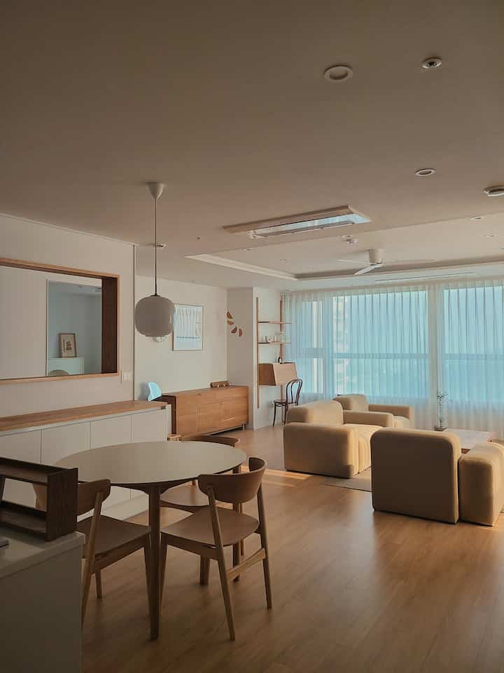 Bright beige and wood-toned living and dining room featuring round dining table and modern sofas with a natural atmosphere