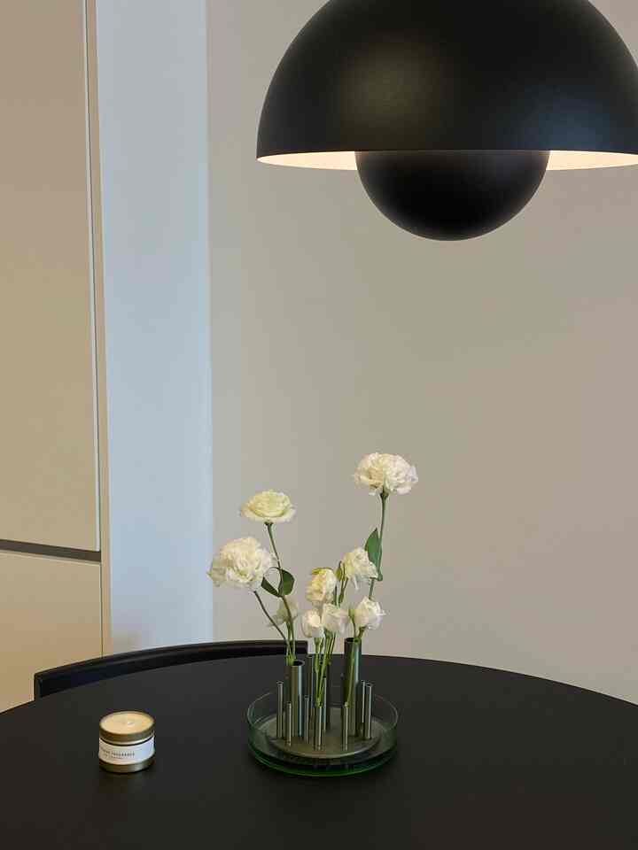 ホワイトとブラックのトーンのダイニングルーム、マットな黒のテーブルと椅子、グリーンの花瓶が配置されたシンプルでモダンな雰囲気のあるインテリア