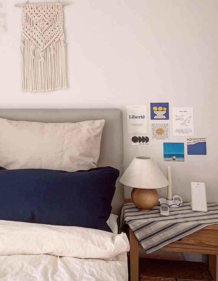 White and natural toned bedroom featuring navy cushions, wood nightstand, and simple wall decor with a calm atmosphere