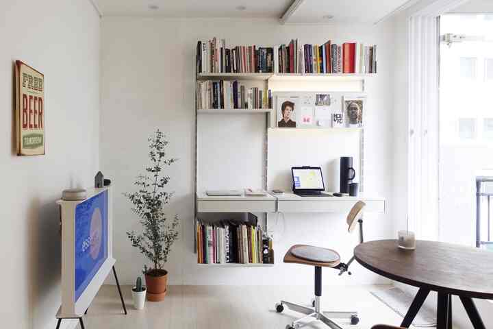 Minimal home office with white and wood tones, featuring tidy bookshelves and a floating desk setup