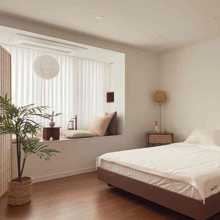 A bedroom with white and wood tones featuring a simple bed and a window seat area, creating a calm and minimal atmosphere