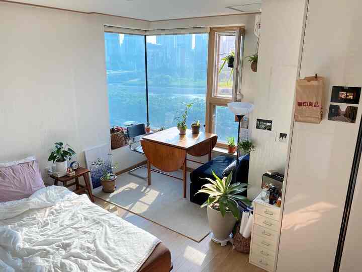 白とナチュラルカラーのワンルーム、木製テーブルと植物が配置された爽やかな夏の雰囲気のある印象的な空間