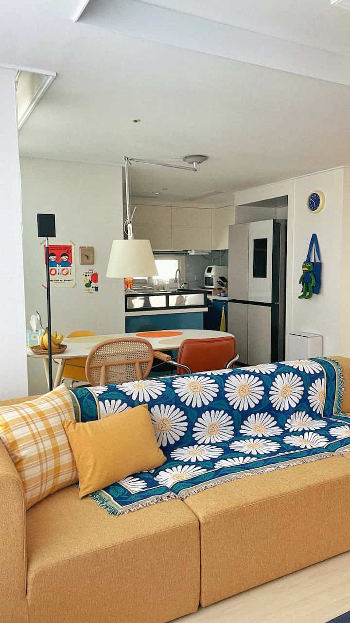 Yellow and navy toned living room and kitchen featuring vintage-style sofa and colorful dining chairs creating a cozy atmosphere