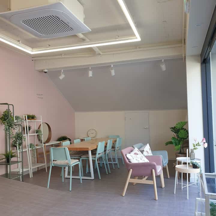 Soft pink and beige small cafe space featuring wooden dining table, mint-colored chairs, and cozy armchairs with natural interior elements