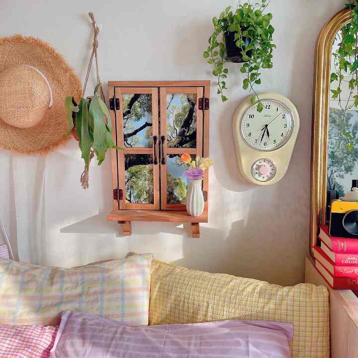 Beige wall with brown wooden shelf, cream wall clock, assorted cushions, and plants in a cozy bedroom space