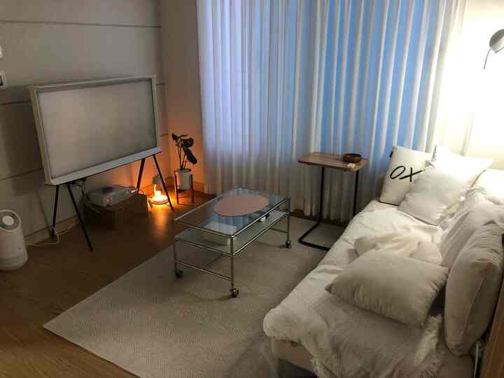 白と木目調のリビング、広いソファとガラスのコーヒーテーブル、サイドテーブルとカーテンが落ち着いた雰囲気を演出する空間