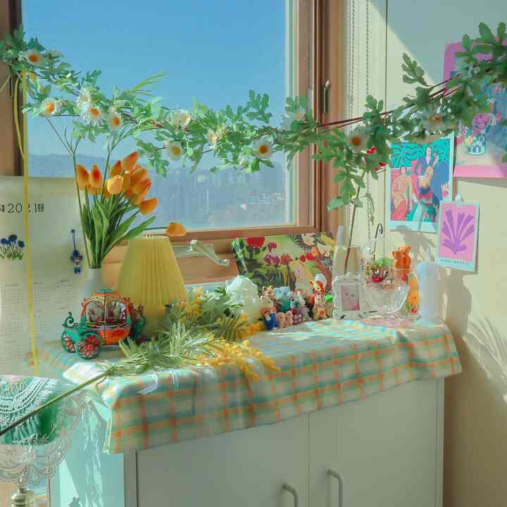 Natural and yellow-toned living room window area featuring white cabinet decorated with vintage ornaments and floral garland, creating a warm cozy atmosphere