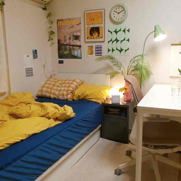 A cozy 5-pyeong studio bedroom in white and pastel green tones, featuring yellow bedding, a desk, and plants