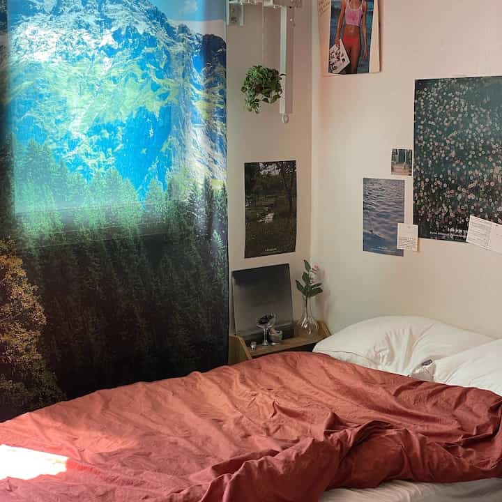 Bedroom with white walls and brown duvet cover, featuring mountain landscape curtain and posters for a natural vibe
