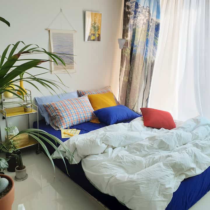 A bright and modern studio kids' room with white and blue tones, featuring checkered cushions and a yellow nightstand