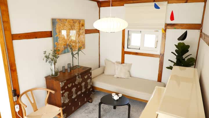 ナチュラルな色調と白い壁の小さなリビング、木製家具とソファが落ち着いた雰囲気を醸し出すインテリア