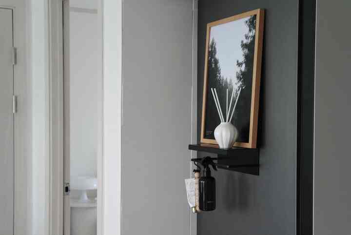 グレーとホワイトのトーンのキッチン壁に黒い棚があり、その上に額縁、ディフューザー、スプレーボトルが並ぶ整った空間