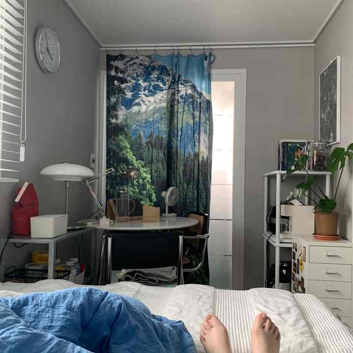 White and gray toned studio bedroom featuring a round dining table, rattan chair, indoor plant, and neat storage furniture in a cozy space