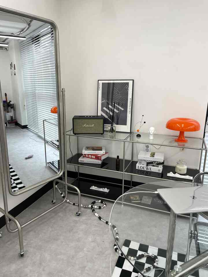 白い壁と黒いメタル棚のあるモダンなリビング、美しいオレンジ色のランプとアートポスターが配置された印象的な空間