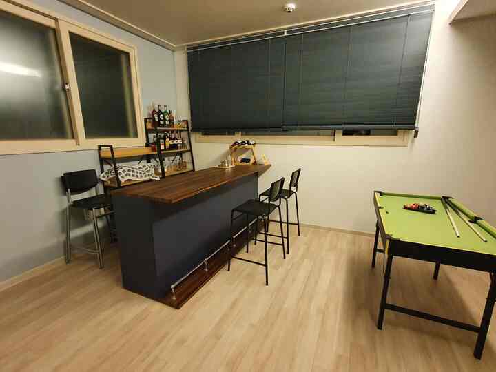 Navy-toned home bar and playroom featuring a wooden bar table with bar stools and a mini pocket billiard table on light brown flooring