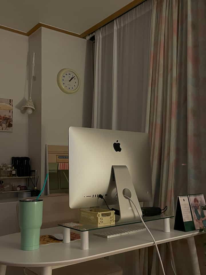 Cozy white and pastel-toned curtains define a studio apartment home office with a clean desk and computer setup