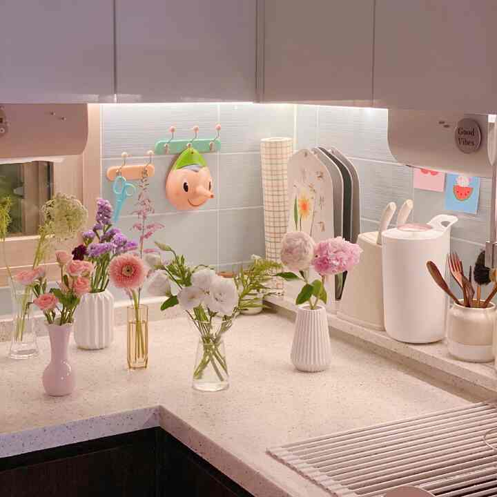 White and pink toned kitchen space featuring beautifully arranged flower subscription bouquets on the countertop creating a cozy atmosphere