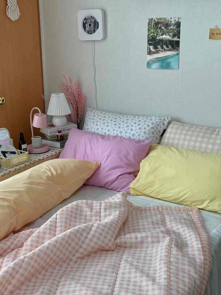パステル調のワンルーム寝室、ピンクのベッドカバーと多彩な枕が配置されたシンプルな空間