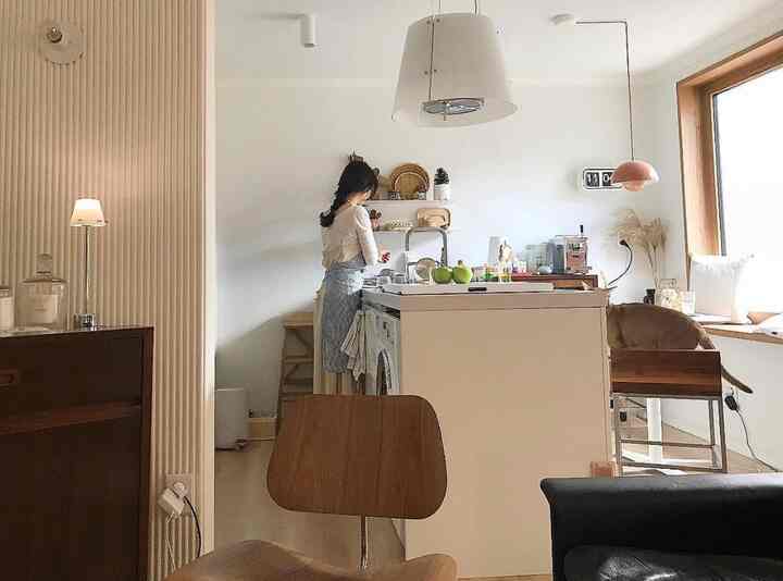 Natural kitchen space with white and wood tones, featuring a kitchen island, multi-purpose shelves, and a cat sitting on a dining chair