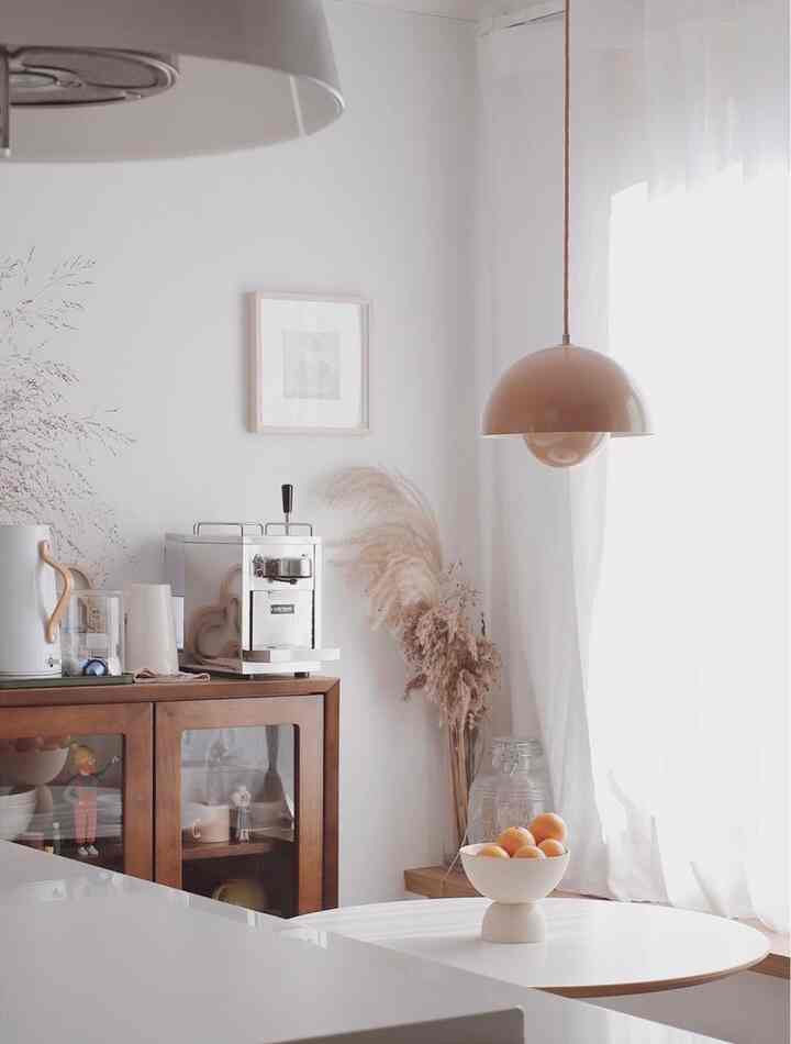 白い壁を背景に木目調のキャビネットが配置され、ペンダントライトとカーテンが調和するシンプルなキッチン空間