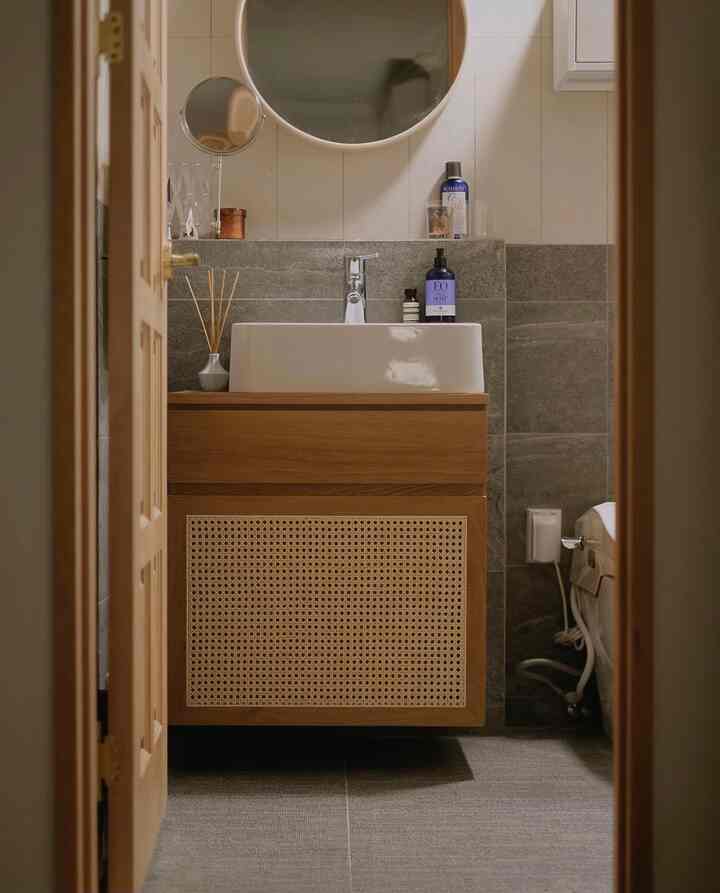 Simple dry bathroom featuring natural wood tones and gray tiled walls, with a round mirror and basin sink setup