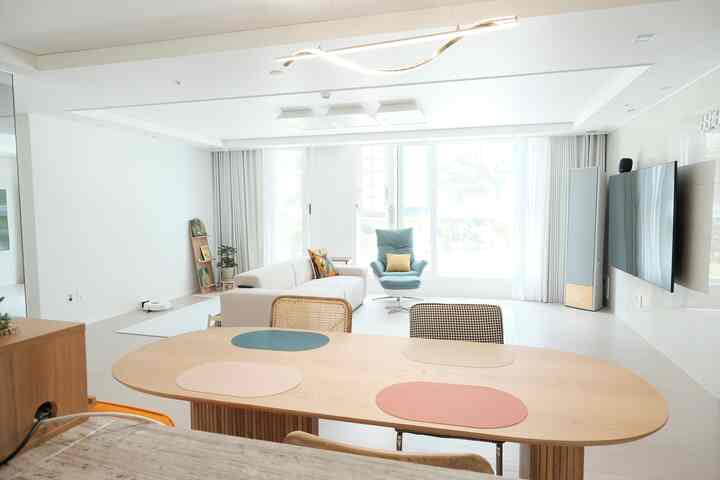 白と木目調のモダンな4人用リビング、自然光が差し込む大きなダイニングテーブル、アームチェア、ソファが配置された空間