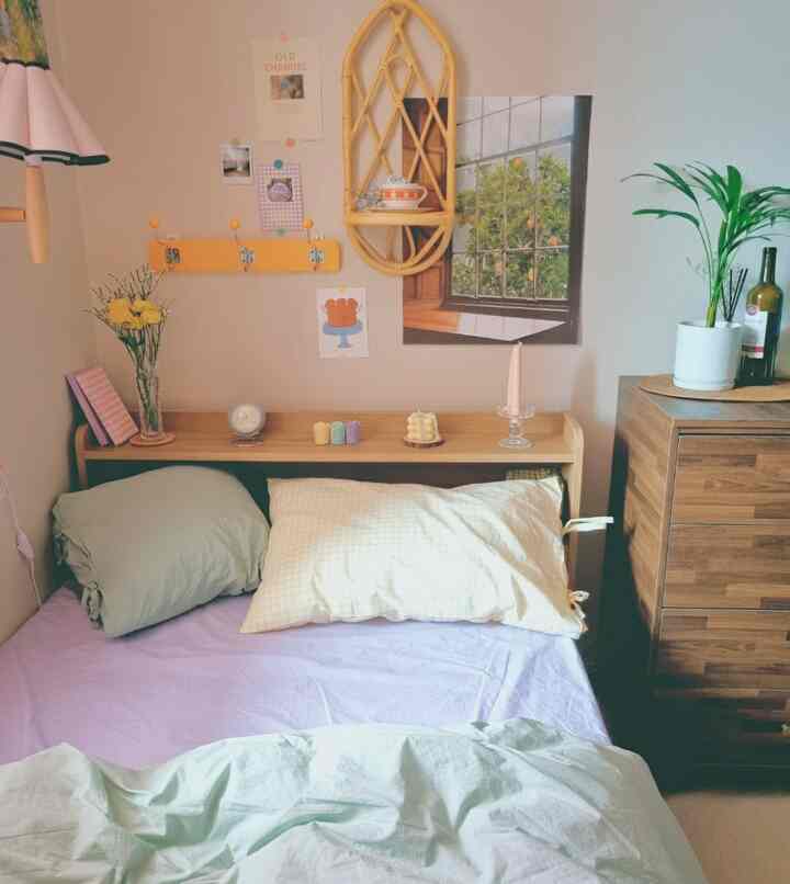 Beige walls and wood-tone furniture in a small bedroom, featuring colorful candles and small objets on the headboard creating a cozy vibe