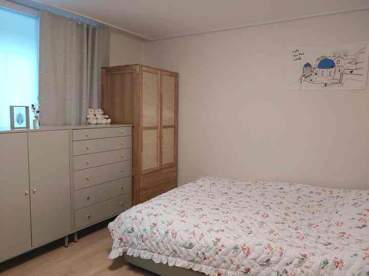 ベージュの壁と木目調のワードローブがあるナチュラルな寝室、花柄の布団が掛かったベッドが配置された落ち着いた空間