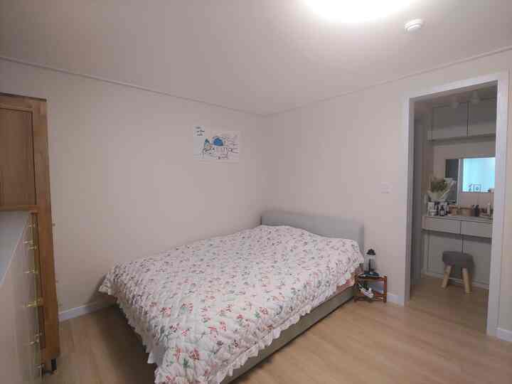 白とライトブラウンのトーンの寝室、ベッドと小さなナイトテーブル、化粧台が配置された落ち着いた雰囲気のインテリア