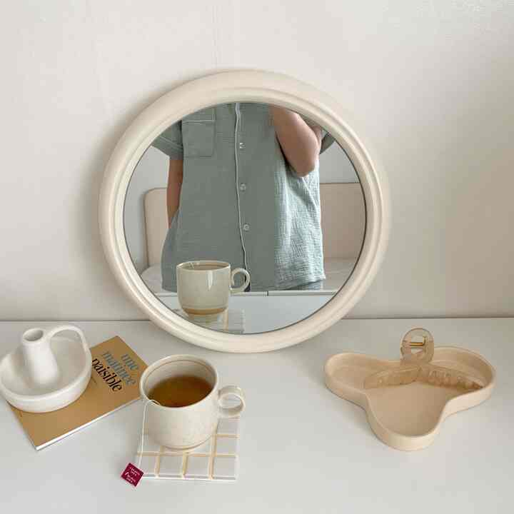 Natural-toned simple bedroom vanity with a round mirror and teacup placed on the table creating a cozy atmosphere