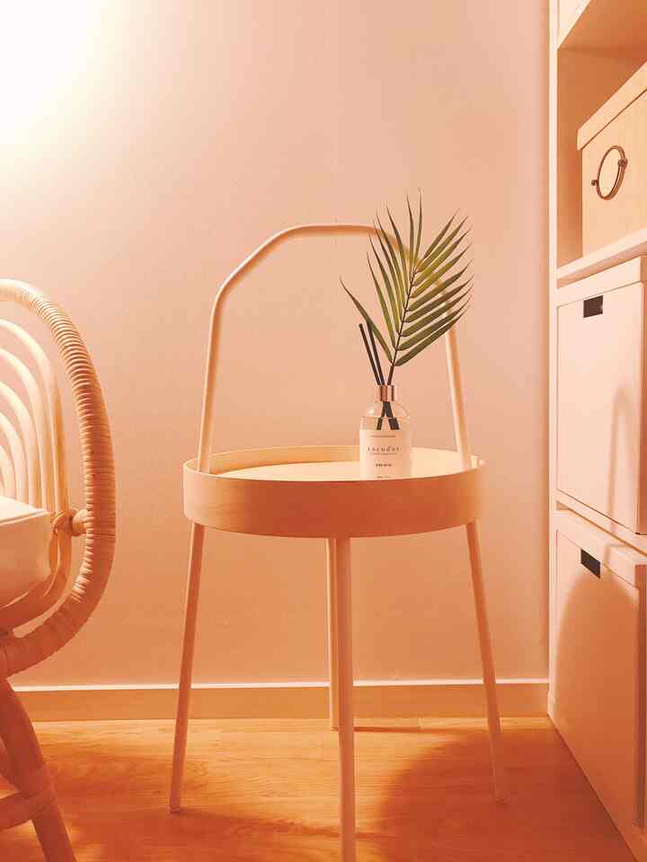 Bright wood tone natural studio apartment relaxation area featuring a rattan armchair and a handled side table with diffuser
