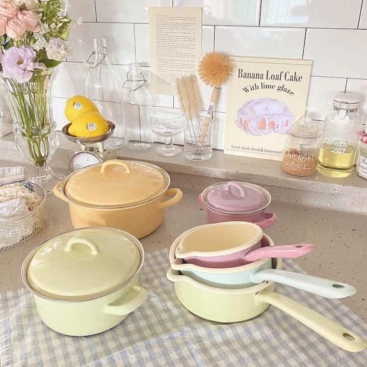 Pastel tone kitchen space featuring colorful enameled pots, lemons, and flower decorations creating a cozy atmosphere