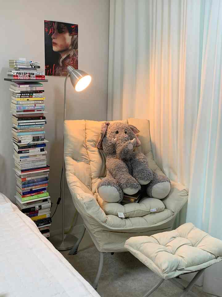 Beige and white toned bedroom reading nook featuring an armchair and stacked books for a cozy atmosphere
